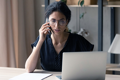 Person talking on phone in office while looking at laptop screen